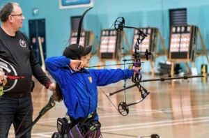 Child shooting an arrow during Indoor archery session with supervisor guiding