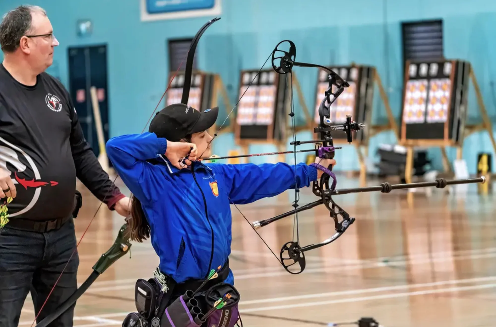 Child shooting an arrow during Indoor archery session with supervisor guiding