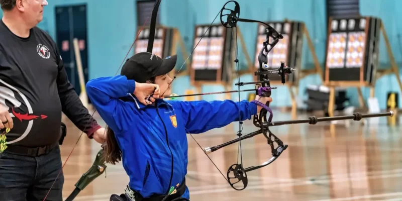 Child shooting an arrow during Indoor archery session with supervisor guiding